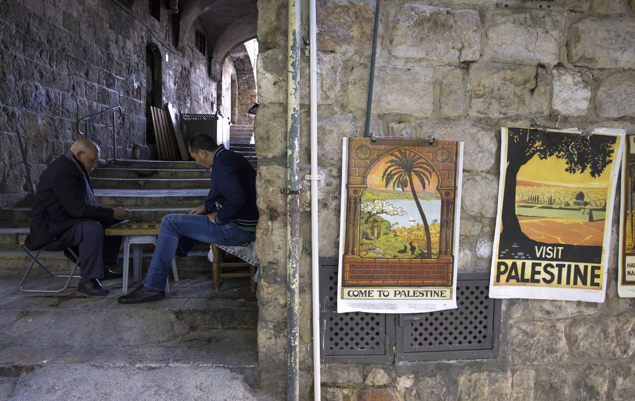 Palestinians in the Moslem Quarter of Jerusalem's Old City pass the time playing dominoes nearby some reproductions of old tourism posters enticing visitors to 'Palestine', on 14 February 2018.  (EPA Photo)