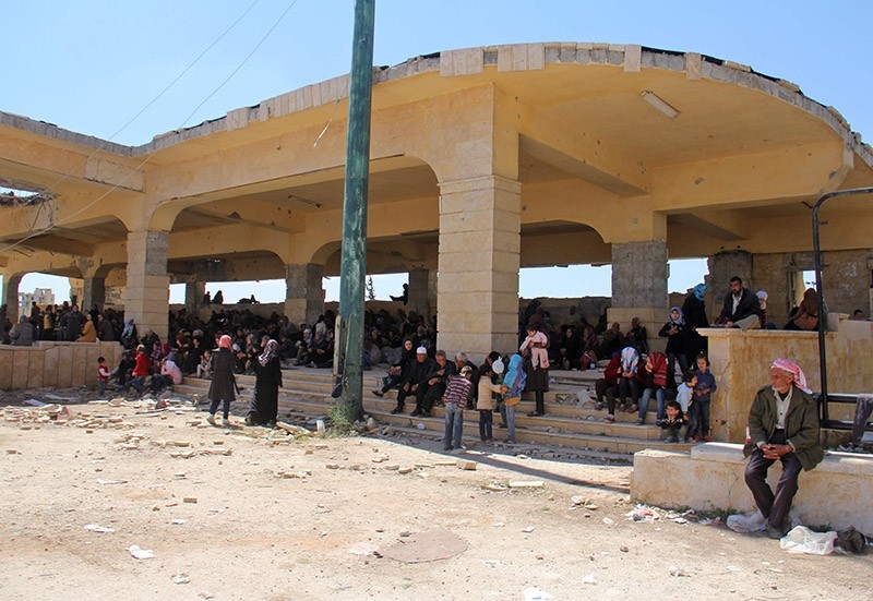 Syrians civilians and pro-regime fighters, from the regime-held towns of Fuaa and Kafraya sit in the shade of a building at the opposition-held transit point of Rashidin, on April 20, 2017, as they wait for the evacuation to resume. (AFP Photo)