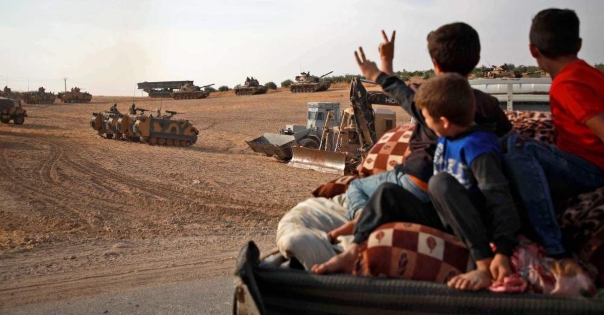  Syrian Arab civilians flash the victory sign as Turkish armored personnel carriers and U.S.-made M60 taks gather in Manbij near the Turkish border, Oct. 14, 2019. (AFP Photo)