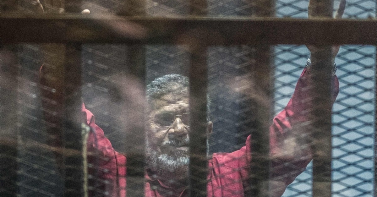 In this file photo taken on April 23, 2016 Egypt's ousted president Mohamed Morsi, wearing a red uniform, gestures from behind the bars during his trial in Cairo at the police academy. (AFP Photo)