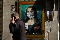 A man holding his mobile phone walks past a poster depicting Leonardo da Vinci's Mona Lisa wearing a protective facemask and holding a mobile phone reading ,Mobile World Virus,, Barcelona, Feb. 18, 2020. (AFP Photo)
