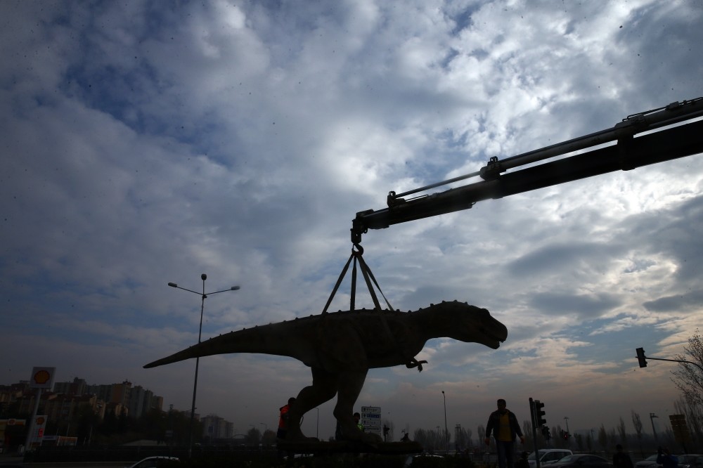 A crane hoists the dinosaur statue.