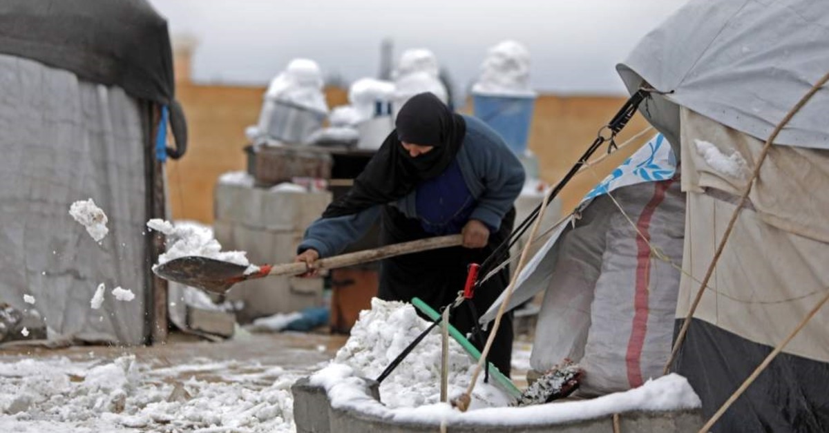 A woman who fled pro-regime forces attacks in northeastern Syria, clears the snow in front of a tent at camp for displaced people in the northern Syrian town of Tal Abyad by the border with Turkey, Feb. 13, 2020. (AFP)