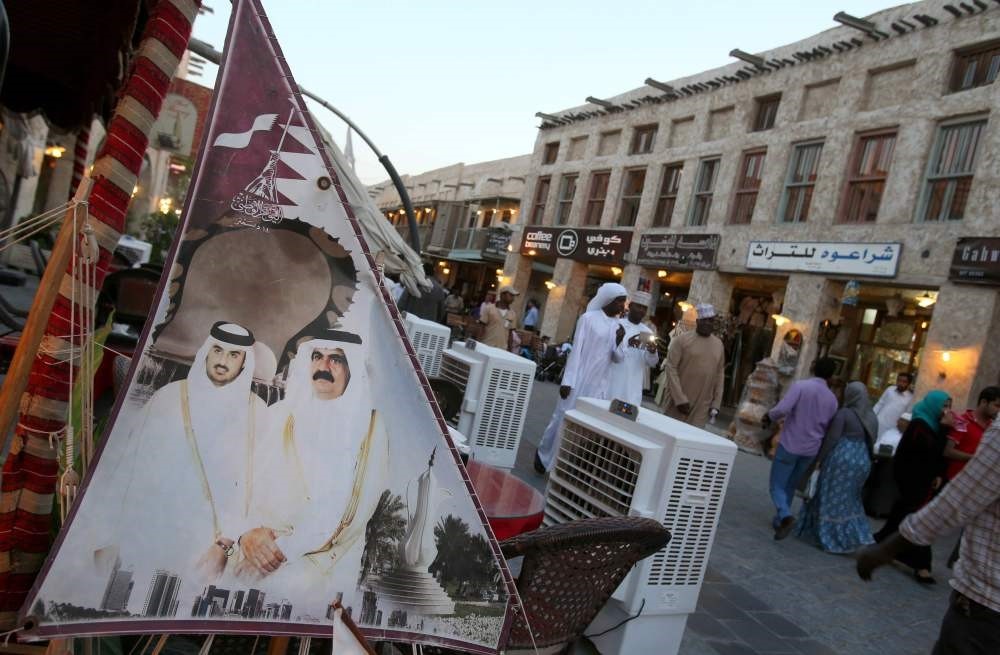 This file photo taken on June 25, 2014 shows people walking past a banner bearing portraits of former emir of Qatar Sheikh Hamad bin Khalifa al-Thani (R) and his son current leader Sheikh Tamim bin Hamad al-Thani displayed at Souq Waqif in Doha.