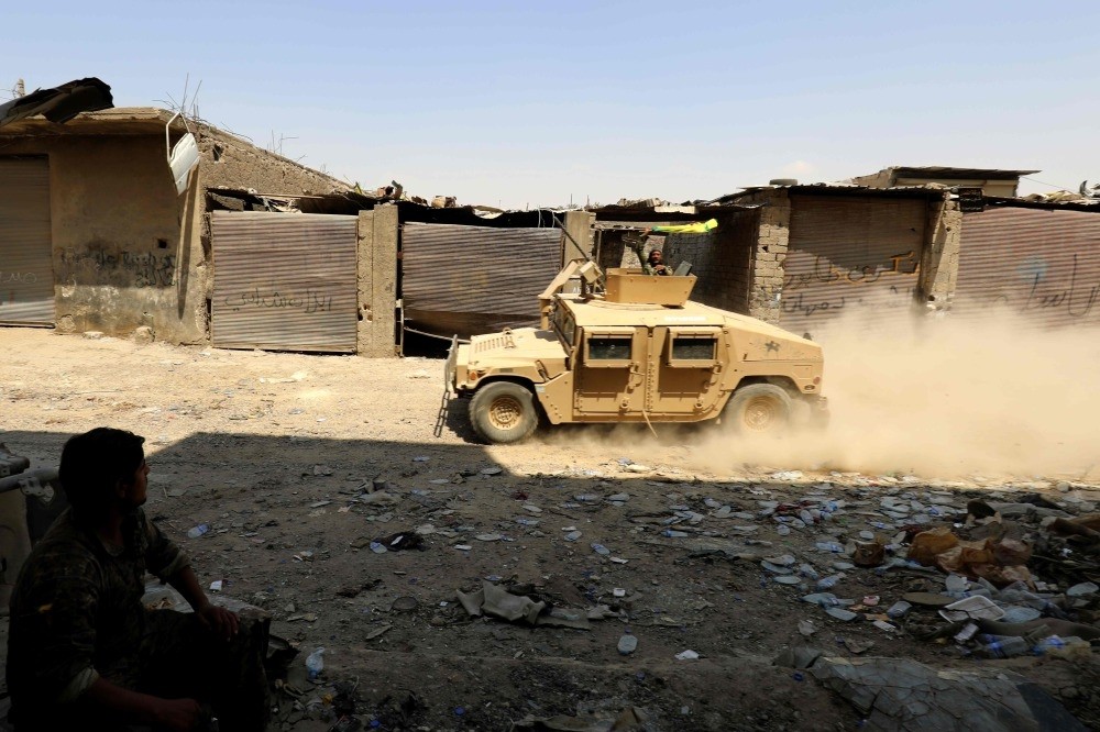 A militant from the U.S.-backed SDF waves a YPG from an armored vehicle driving through the eastern al-Sanaa neighborhood, Raqqa, on the edge of the old city, Aug. 13.