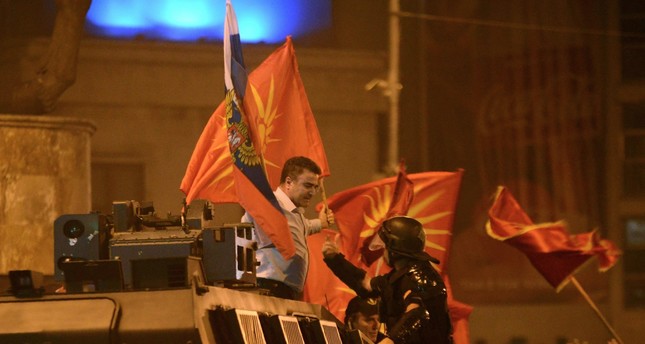 A police officer tries to grab a protester waving former Macedonian and Russian flags atop an armored police vehicle during protests in front of Parliament, Skopje, June 17.