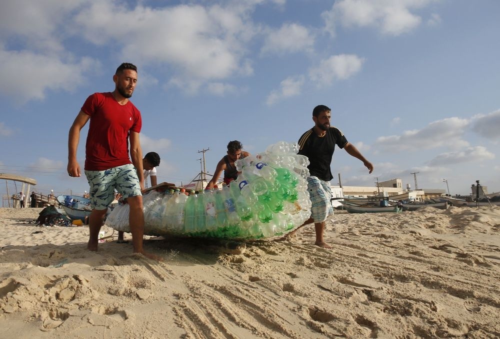 Palestinian fisherman Mouad Abu Zeid (R) and his friends carry his boat that he made from 700 empty plastic bottles on a beach in Rafah, Gaza.
