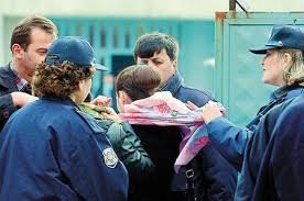 Police officers pull down the headscarf of a young student.