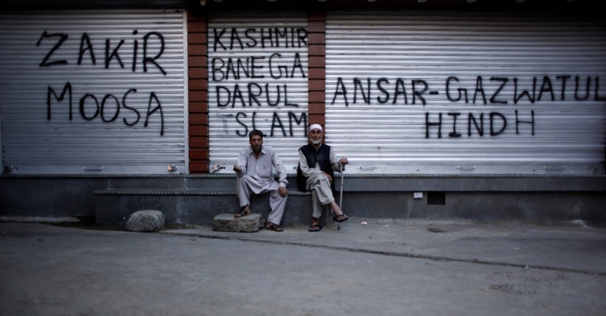 Kashmiri men sit in front of the closed shops painted with graffiti during restrictions after scrapping of the special constitutional status for Kashmir by the Indian government, in Srinagar, Aug. 20, 2019. (Reuters Photo)