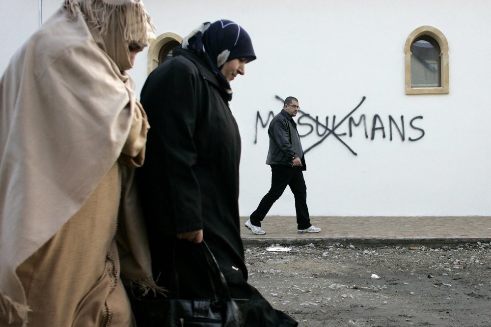 Muslim residents walk past anti-Islam graffities painted on the walls of a mosque in the town of Saint-Etienne, central France,  Feb. 8, 2010. 