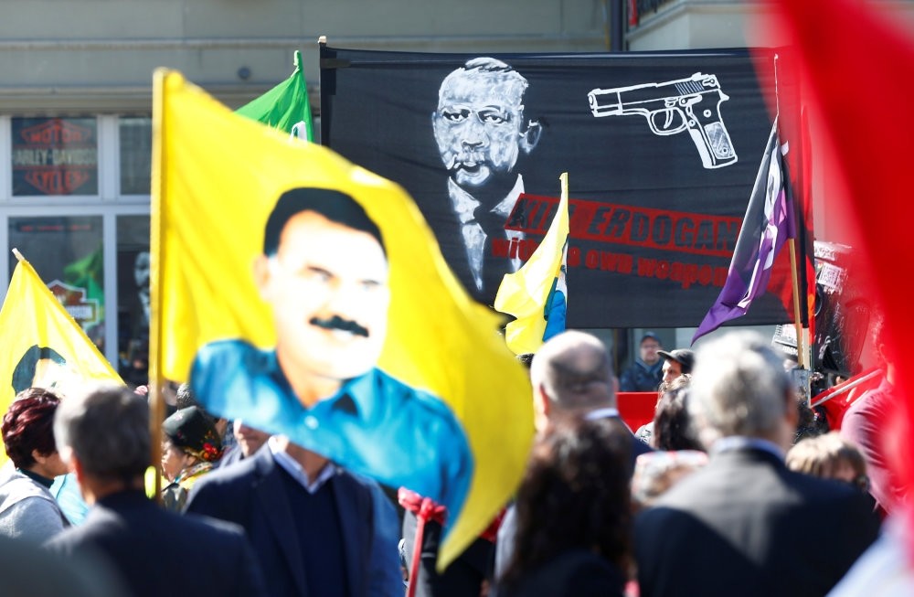 PKK supporters holding a placard picturing President Erdou011fan with a gun pointed to his head and a flag picturing imprisoned PKK leader, Abdullah u00d6calan, along with the terrorist group's flags during the demonstration in Swiss city of Bern, March 25.