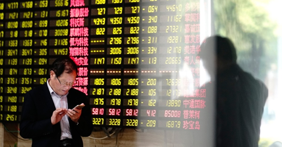 A man looks at his smartphone near a display showing stock prices at a brokerage house in Shanghai Monday, May 6, 2019. (AP Photo)