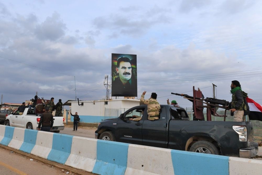 A convoy of pro-Syrian regime fighters seen as they ride through the windows of pickup trucks upon arriving in Syria's northern region of Afrin, with a portrait of the PKK leader on a banner in the background, Feb. 20.