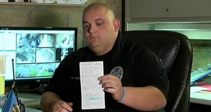 This screenshot from an AP video shows Sperry Police Chief Justin Burch holding his ticket.