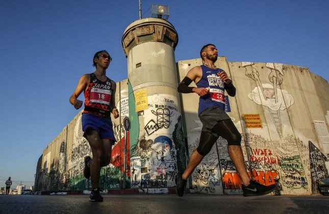 Runners pass by the Israeli separation barrier during the Palestine Marathon, in the West Bank city of Bethlehem, Friday, March 22, 2019. (AFP Photo)