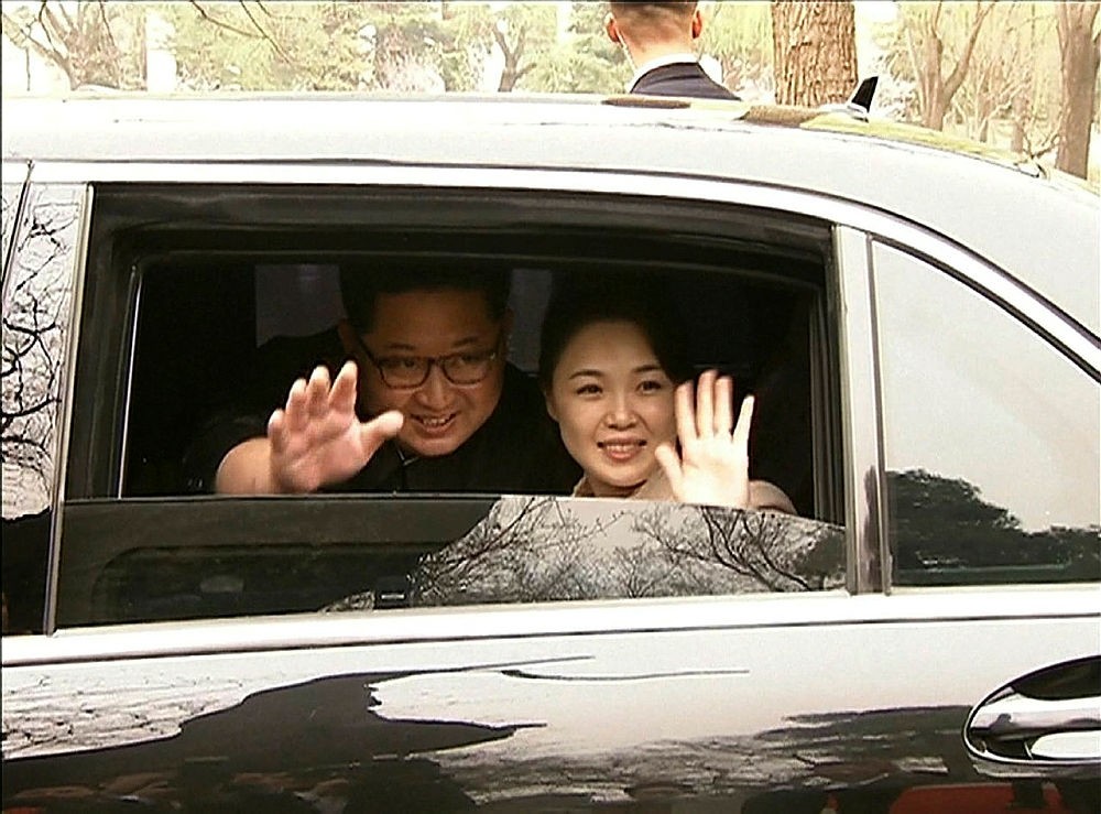 This video grab taken from footage released by China Central Television (CCTV) on March 28, 2018 shows North Korea's leader Kim Jong Un (L) and his wife Ri Sol Ju (R) waving goodbye as they depart by car following a meeting with China's President Xi Jinping in Beijing this week