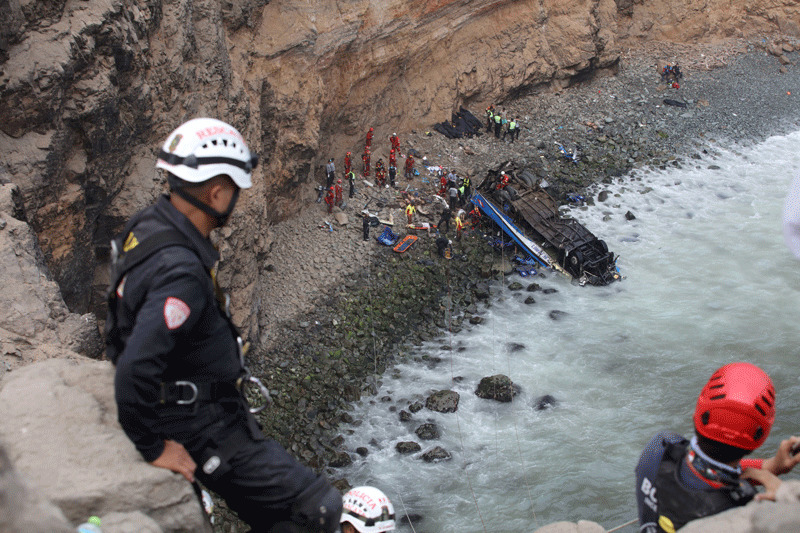 Rescue workers stand at the scene after a bus crashed with a truck and careened off a cliff along a sharply curving highway north of Lima, Peru (Reuters Photo)