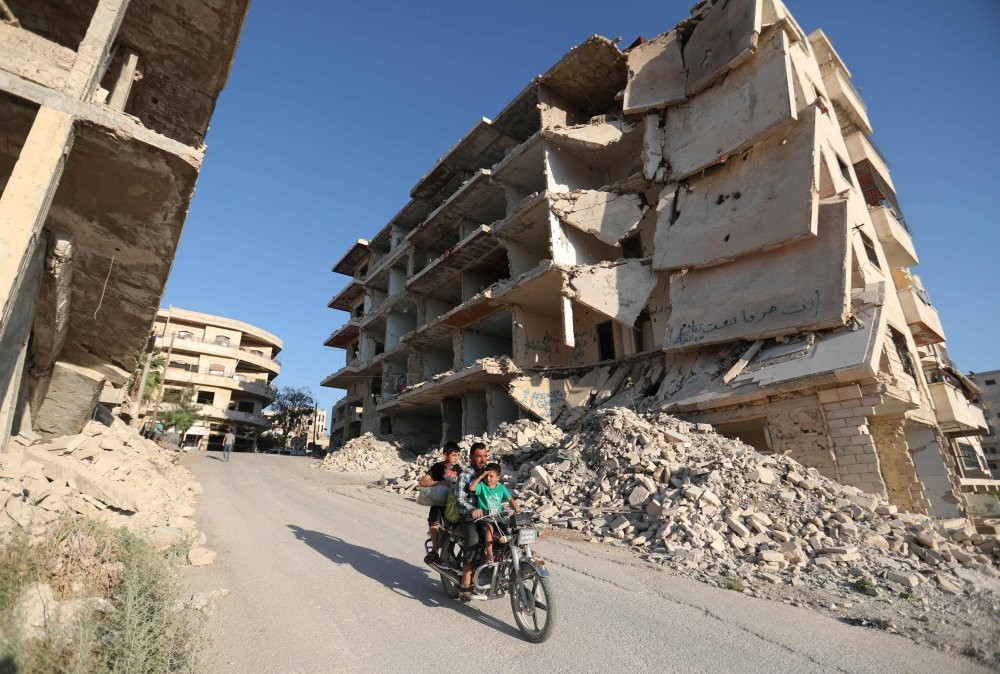 Syrian men ride a motorcycle past heavily-damaged buildings in Idlib province, Sept. 27.