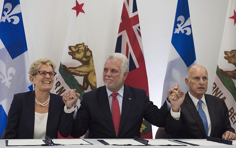 Quebec Premier Philippe Couillard, flanked by Ontario Premier Kathleen Wynne, left, and California Gov. Jerry Brown, raise their hands after signing an agreement on climate change in Quebec City, Canada  on Friday, Sept. 22, 2017 (AP Photo)