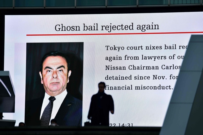 A pedestrian walks past an electric board showing a news program displaying a picture of former Nissan chief Carlos Ghosn in Tokyo on January 22, 2019 (AFP Photo)