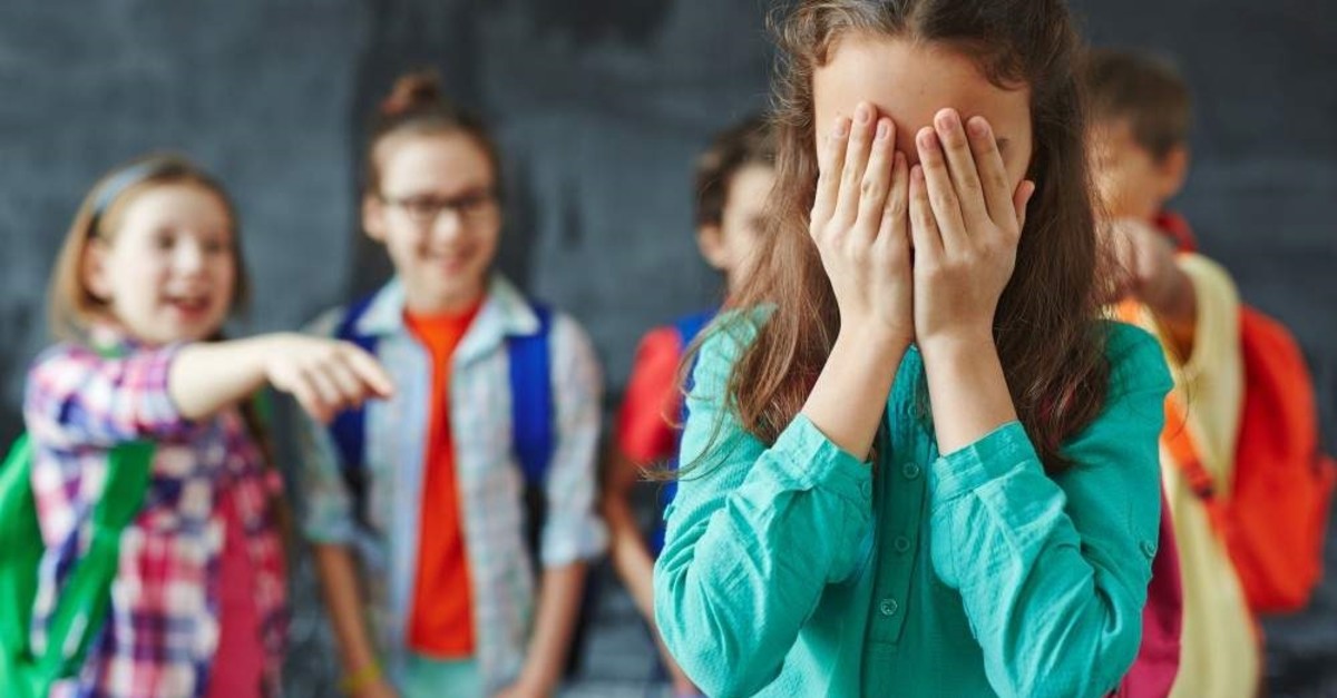 Schoolgirl crying on background of classmates teasing her. (iStock) 