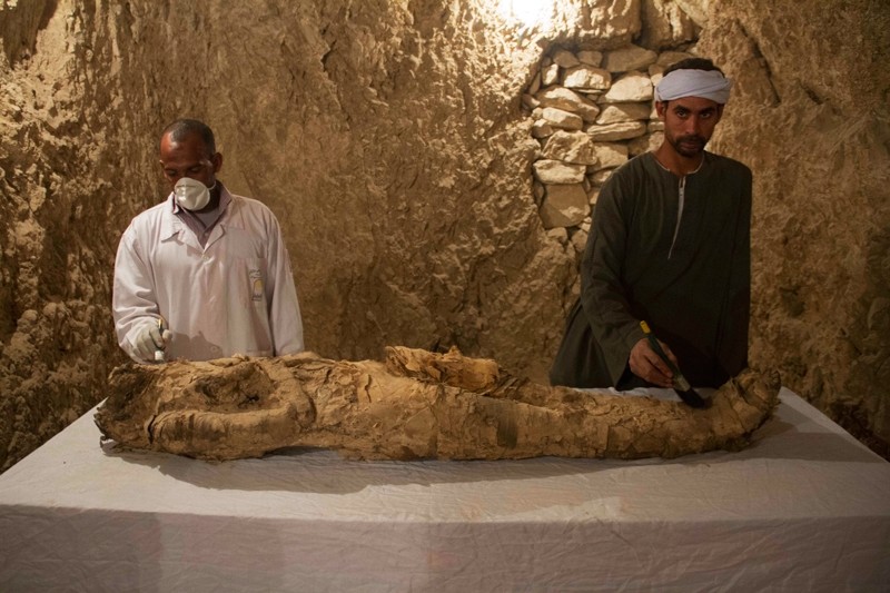 Egyptian excavation workers restore a mummy in a newly discovered tomb in Egypt's Luxor ( AP Photo) 