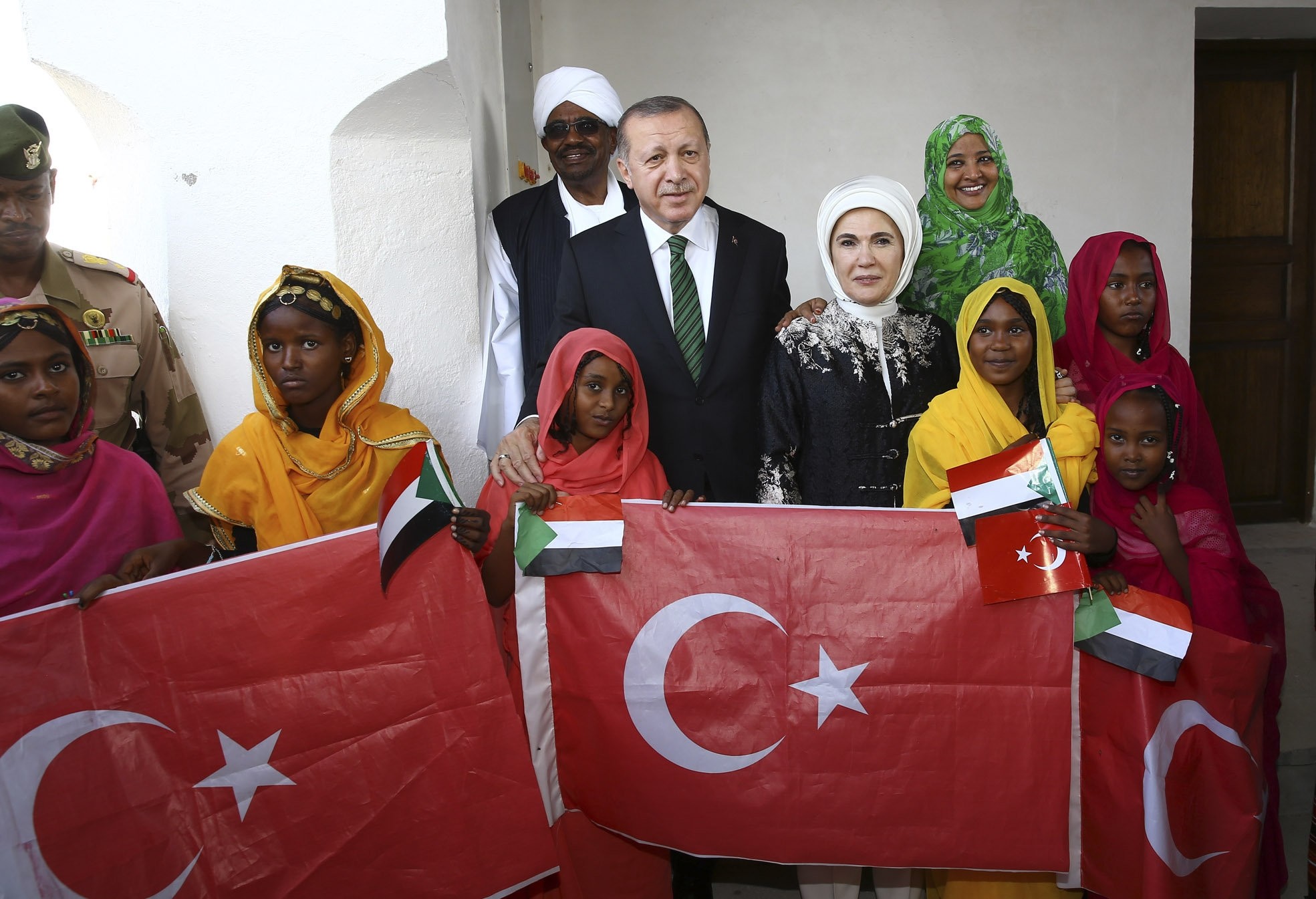 President Erdou011fan (C), accompanied by first lady Emine Erdou011fan, pose for a photograph with Sudan's President Omar al-Bashir and first lady Widad Babiker u00d6mer Modawi alongside local people holding the Sudanese and Turkish flags in Port Sudan, Dec. 25,