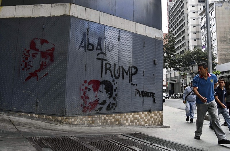 A man walks near a grafitti depicting late Venezuelan president Hugo Chavez (R and L), President Nicolas Maduro (C) with a legend reading ,down with Trump, in Caracas, on Jan. 24, 2019. (AFP Photo)