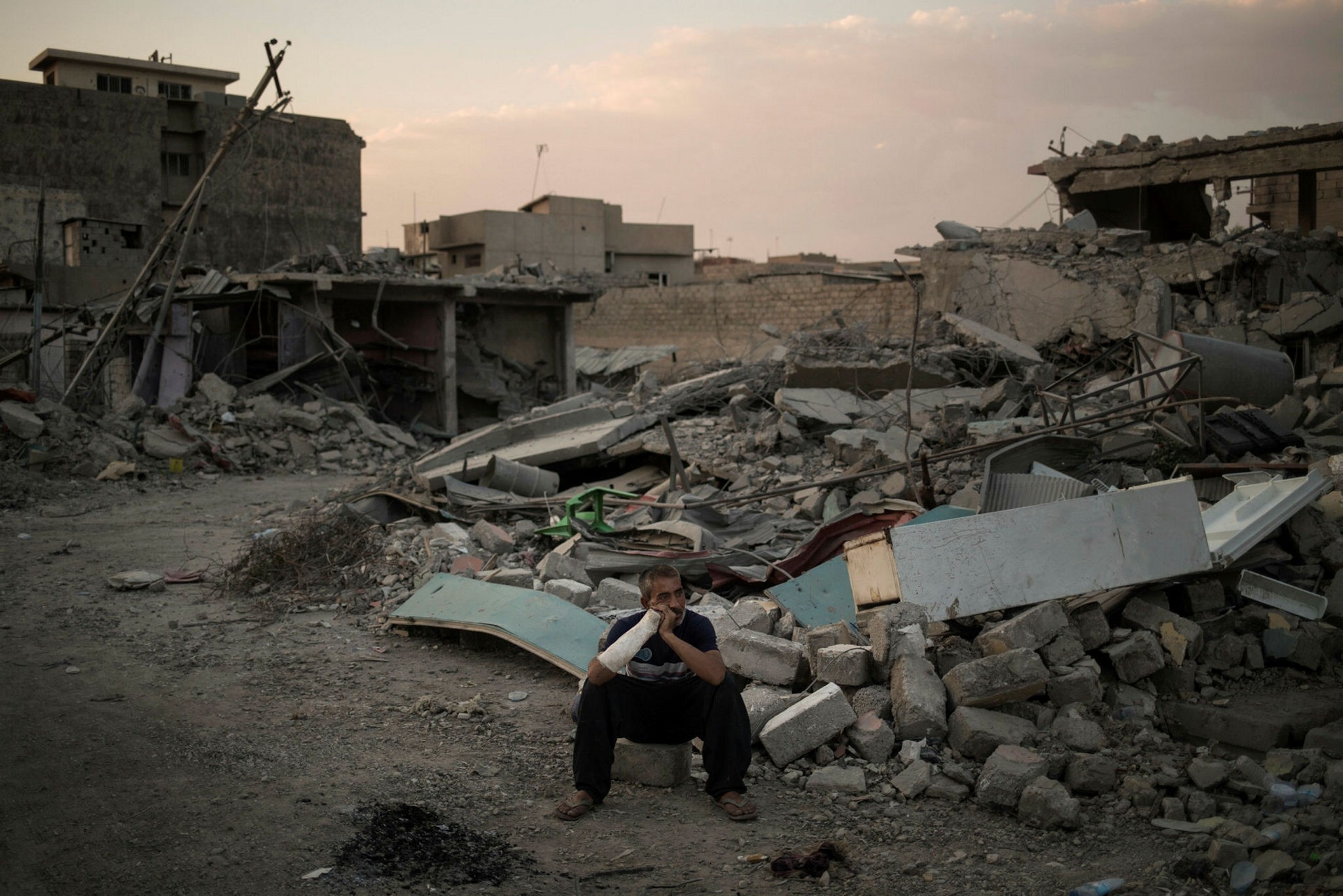 A man who was injured when his house was hit by an explosion sits on his damaged street on the west side of Mosul, July 13.