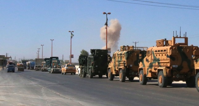 A plume of smoke rises above buildings during an air strike by Syrian regime forces as a Turkish military convoy passes through Maarat al-Numan in Syria's Idlib reportedly heading toward the town of Khan Sheikhoun, on August 19, 2019. (AFP Photo)