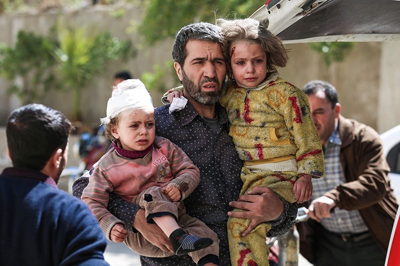  A Syrian man carries two injured children after a reported air strike in the opposition-controlled town of Hamouria