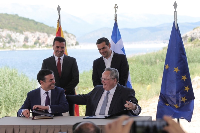 Greek PM Tsipras (background-R) and his Macedonian counterpart Zaev (background-L) look on as Greek FM Kotzias (R) and his Macedonian counterpart Dimitrov sign an agreement on Macedoniau2019s new name in the village of Psarades; Prespes, Greece, June 17.