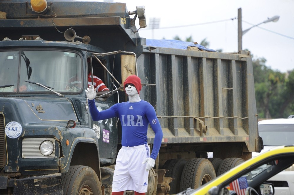 A young Liberian man stands in the sweltering heat for hours, painted head to toe in the colours of the national tax authority, at a traffic junctions.