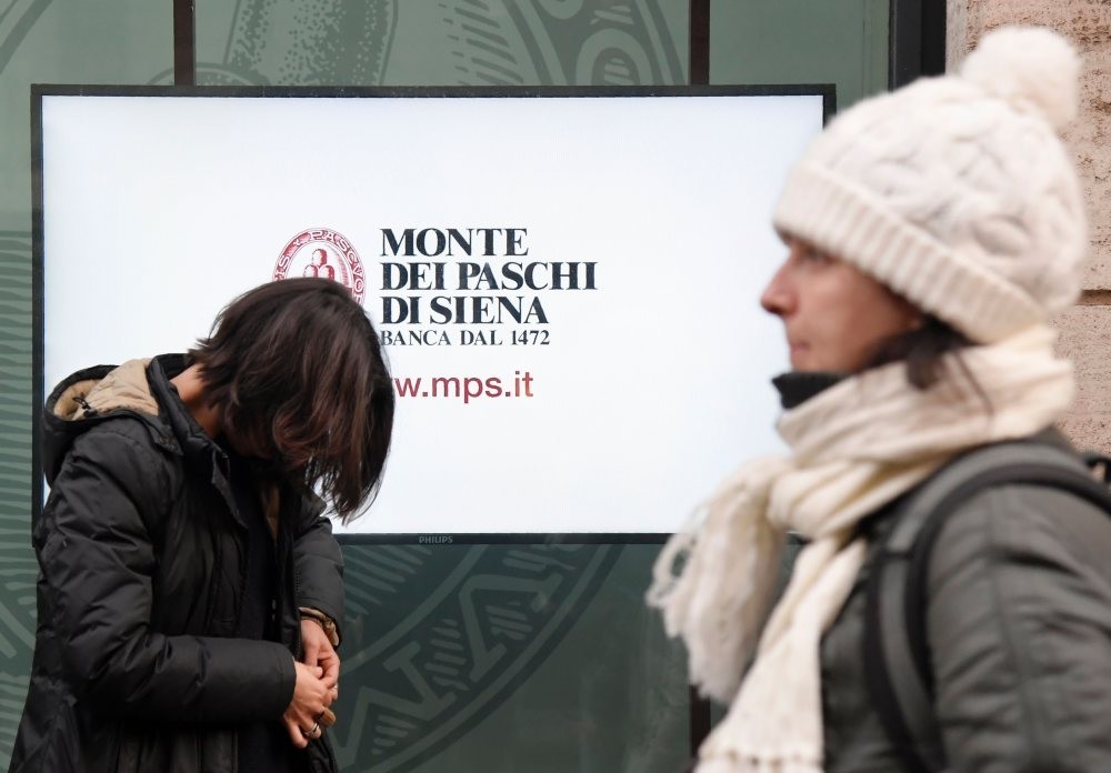 People walk past an office of Italian bank Monte Dei Paschi Di Siena.