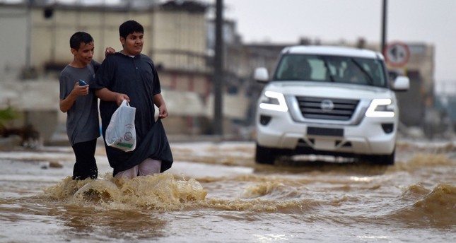 الشباب يسيرون في شارع غمرته المياه بعد هطول أمطار غزيرة في مدينة جدة الساحلية السعودية في 24 نوفمبر/ تشرين الثاني 2022 AFP