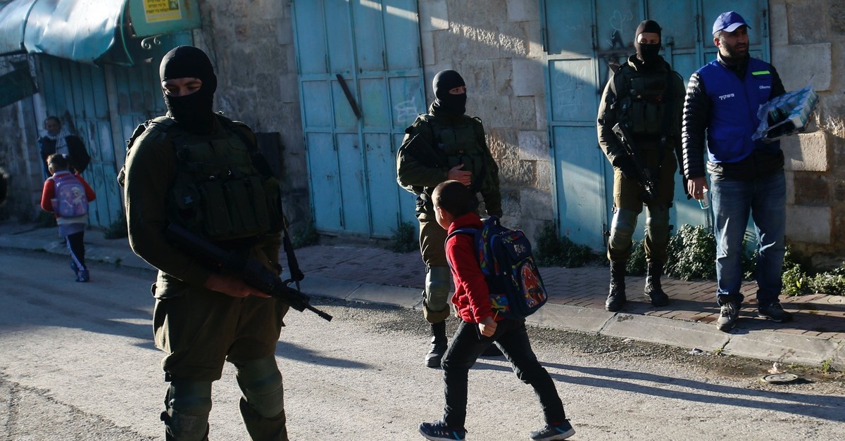 Palestinian children walk past Israeli soldiers on their way to school in the West Bank city of Hebron, Feb. 12, 2019.