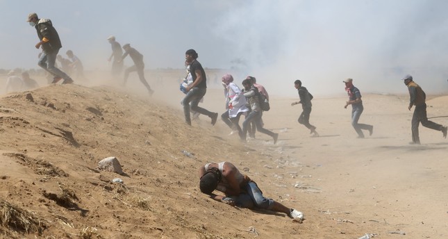 A Palestinian demonstrator reacts as others run from tear gas fired by Israeli forces during a protest marking the 70th anniversary of Nakba, at the Israel-Gaza border in the southern Gaza Strip yesterday.