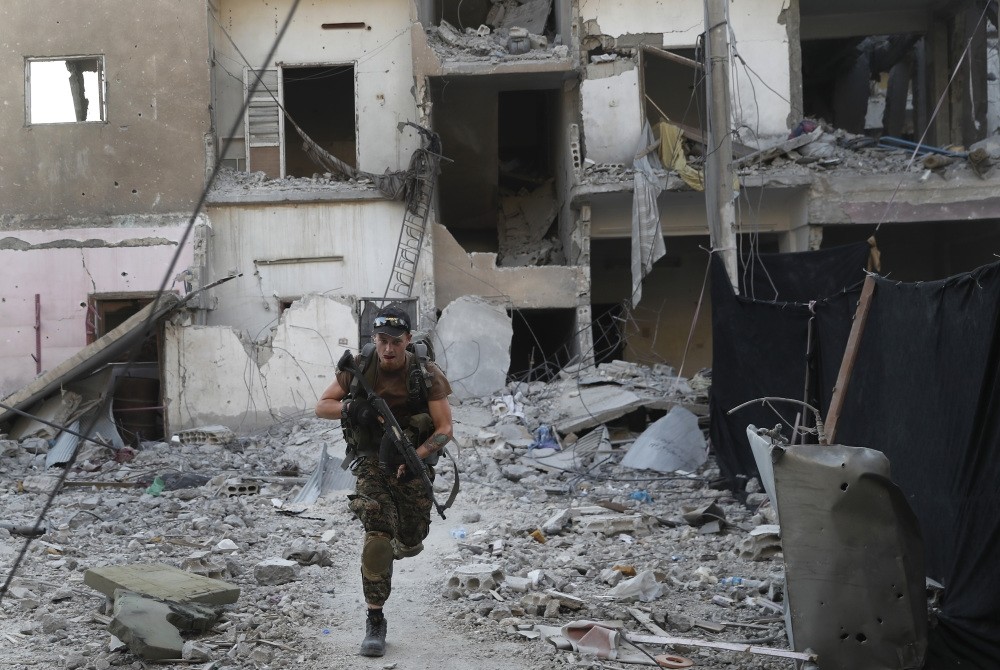 A U.S.-backed YPG terrorist runs in front of a damaged building as he crosses a street on the front line in Raqqa, Syria, July 27. 