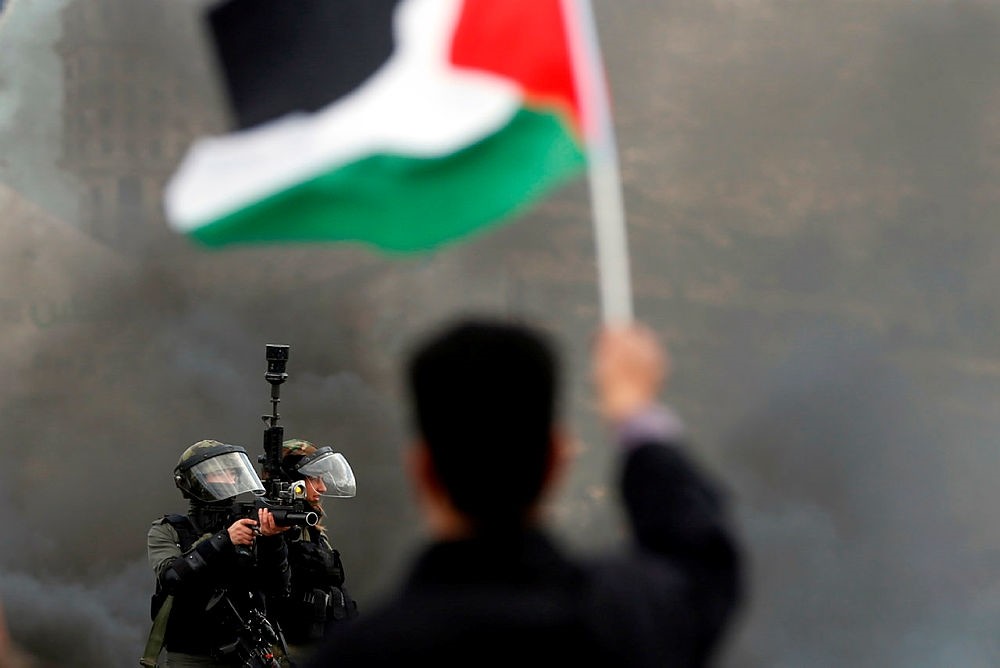 Israeli border guards take aim as a Palestinian protester waves the national flag during clashes following a demonstration in the West Bank city of Ramallah, March 9, 2018. (AFP Photo)