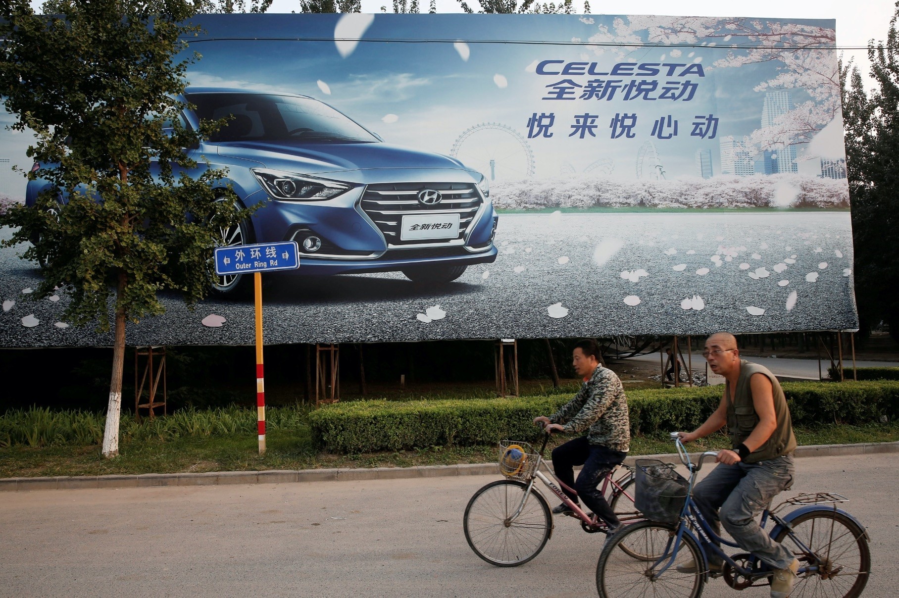 Men cylce past an advertising billboard for Hyundai cars opposite the plant of Hyundai Motor Co in Beijing.
