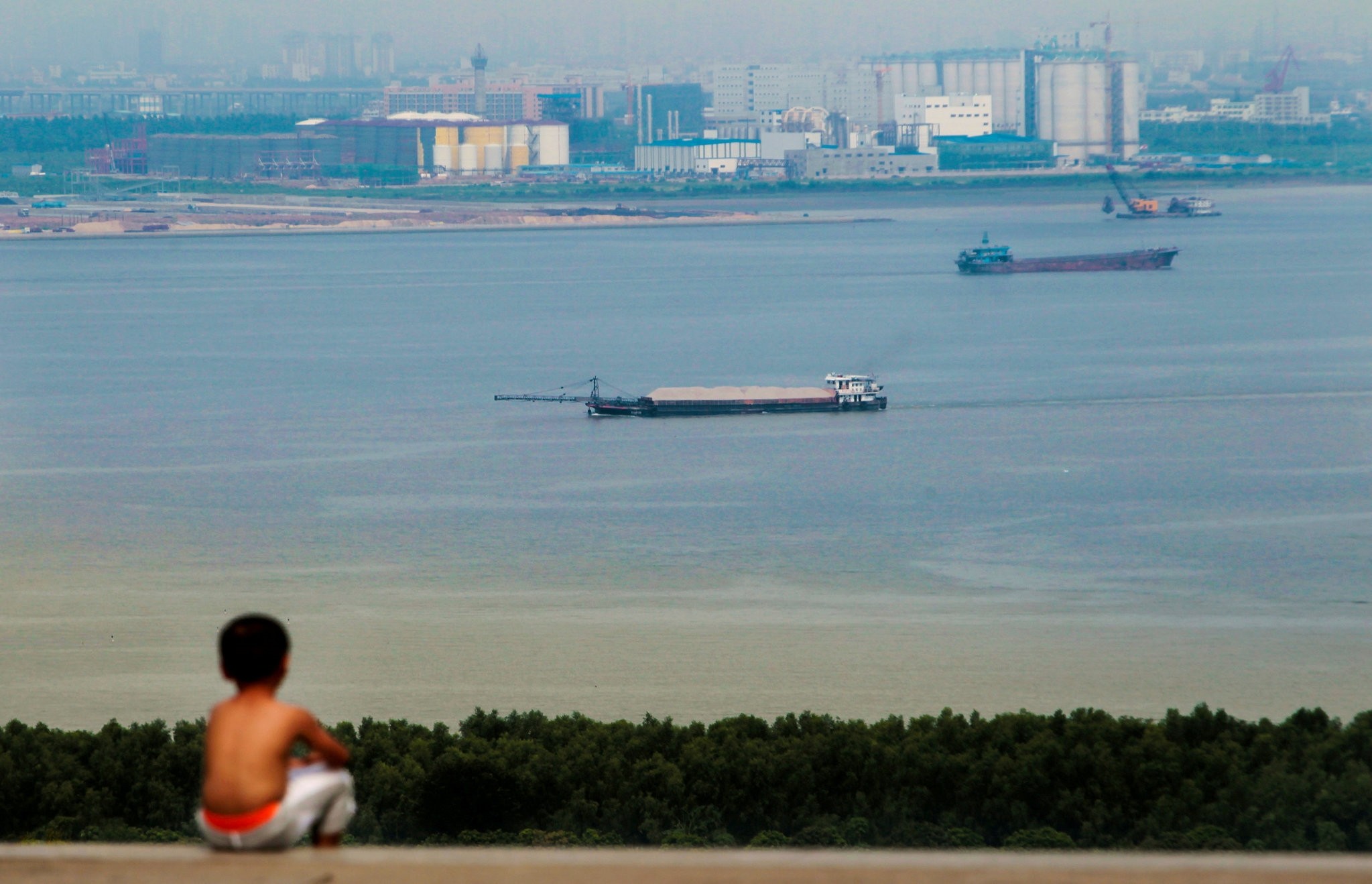 A boy looks at cargo ships passing along the Pearl River in Guangzhou, Guangdong province, Aug. 6, 2014.
