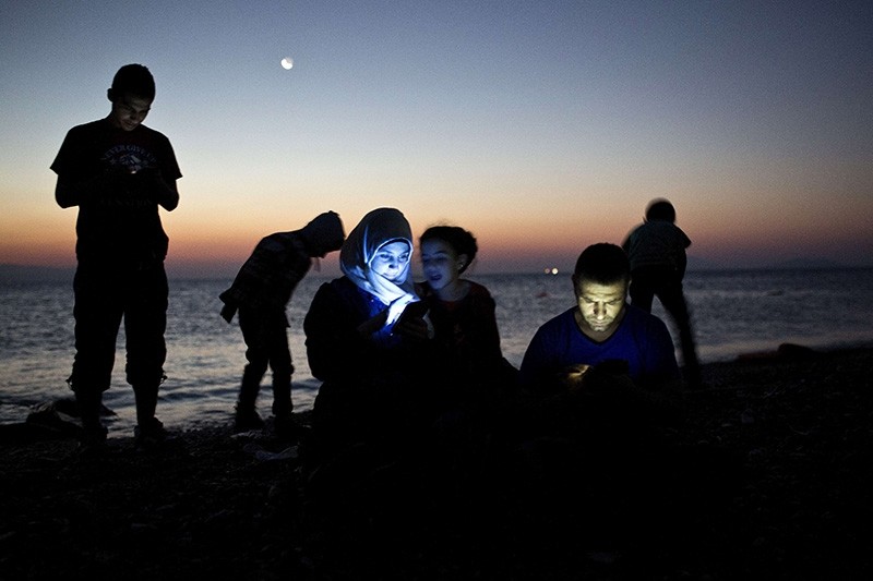 Migrants check their mobile phones after getting out of an inflatable boat on a beach on the Greek island of Kos, after crossing a part of the Aegean Sea between Turkey and Greece, on Aug. 12, 2015. (AFP Photo)