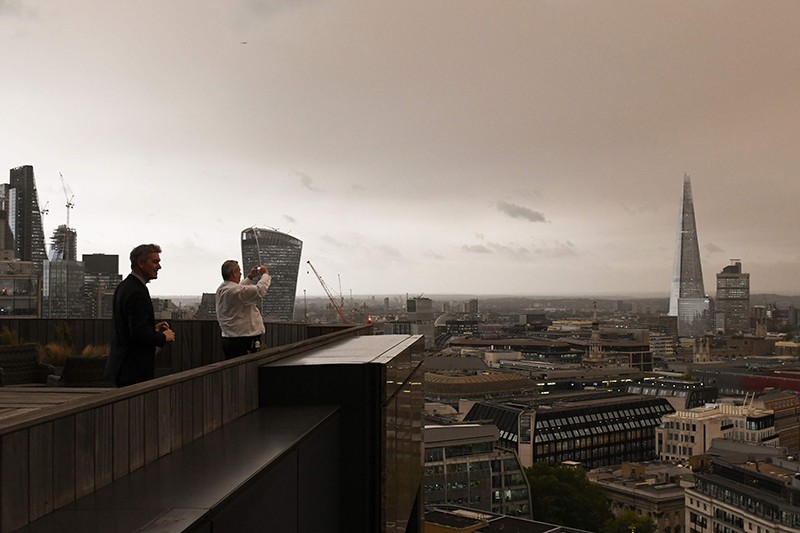 Office workers stand on their balcony to photograph the darkened sky over London on October 16, 2017 caused by warm air and dust swept up by storm Ophelia. 