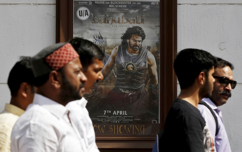 People walk past a poster of the Indian movie u201cBaahubali: The Beginningu201d outside a movie theater in New Delhi. (Reuters Photo)