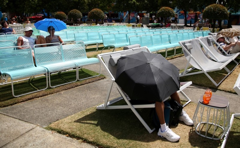 Spectators protect themselves from the heat with umbrellas as they watch tennis on a large video screen in Garden Square at the Australian Open tennis championships in Melbourne, Australia, Jan. 25, 2019. (AP Photo)