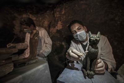 An Egyptian archaeologist cleans a bronze ancient sitting cat statue during a demonstration of a new discovery made by an Egyptian archaeological mission through excavation work carried out since April near the King Userkaf pyramid complex in Saqqara Necropolis, on Nov. 10, 2018. (AFP Photo)