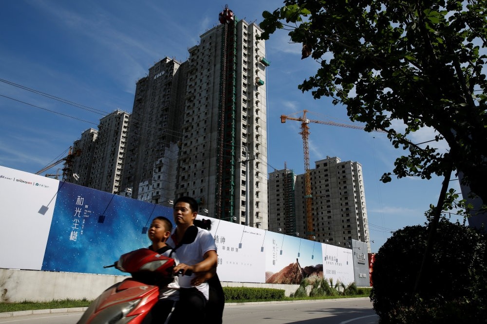 A man and a boy ride an electric scooter past the shells of apartment blocks outside a construction site in Beijing.