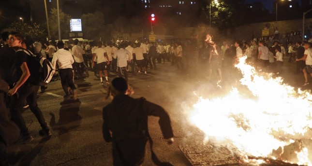 Ultra-orthodox Jews run as members of the Israeli Ethiopian community block the main entrance to Jerusalem on July 2, 2019, to protest the killing of Solomon Tekah, a young man of Ethiopian origin who was killed by an off-duty police officer. (AFP)