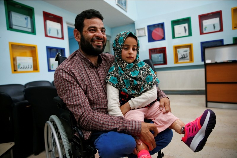 In this Thursday, July 5, 2018 photo, Maya Meri sits on her father Mohammed's lap after being fitted with prosthetic legs at a rehabilitation clinic in Istanbul, Turkey. (AP Photo)