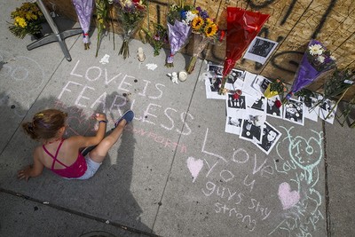 A young girl writes a message on the sidewalk at a site remembering the victims of a Sunday evening shooting on Danforth Avenue, in Toronto on Monday, July 24, 2018. (AP Photo)